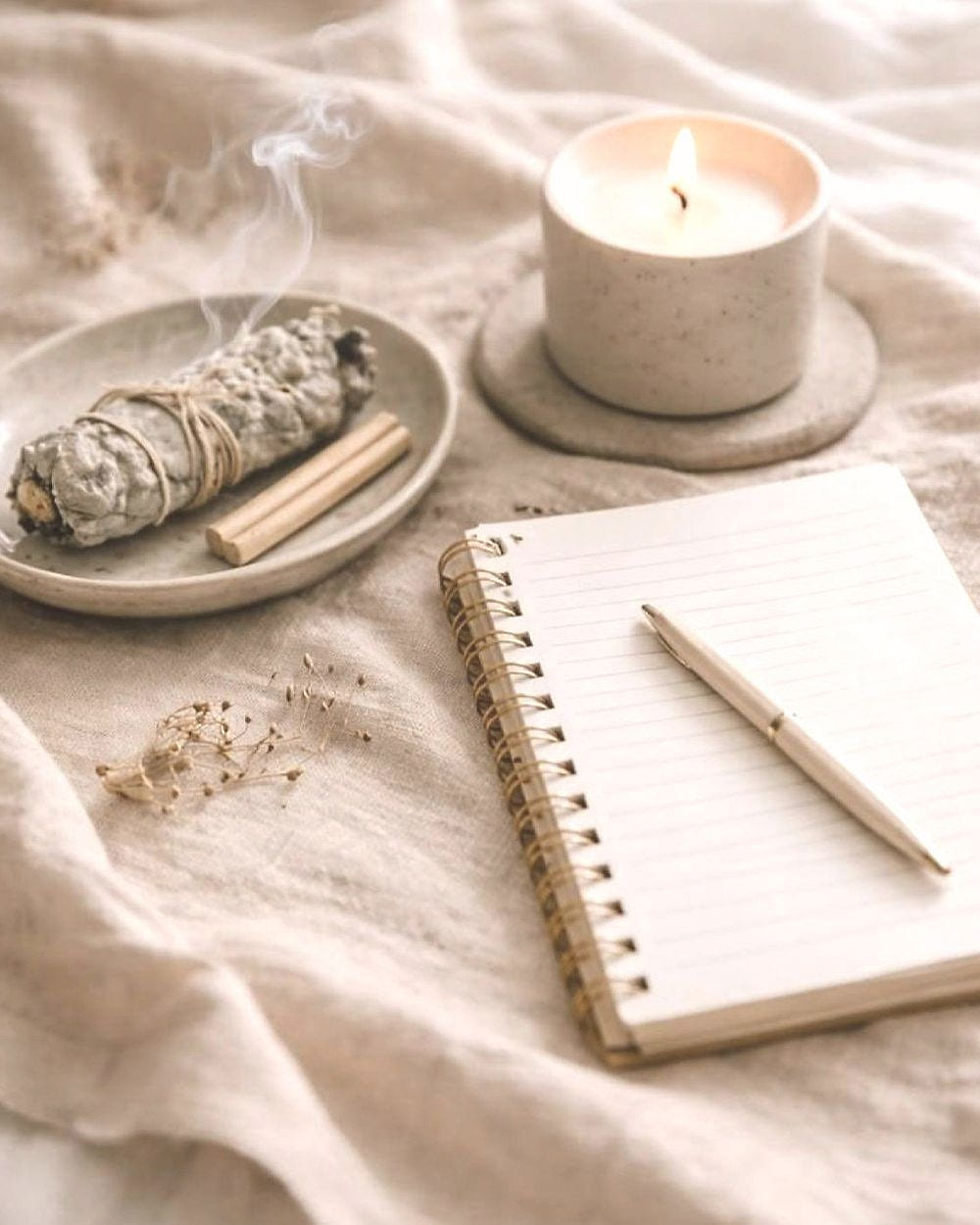 Un cuaderno abierto con un bolígrafo, una vela encendida y un atado de salvia sobre lino